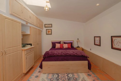 Cozy bedroom with a purple bedspread, wooden furniture, and warm lighting, featuring a skylight and decorative artwork.