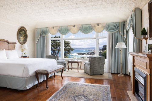 A luxurious hotel room with a king bed, seating area, and large windows showcasing a scenic ocean view.