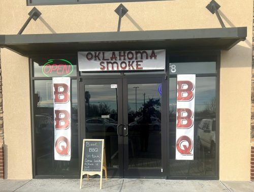 Front entrance of Oklahoma Smoke BBQ restaurant with an open sign and a chalkboard advertising specials.