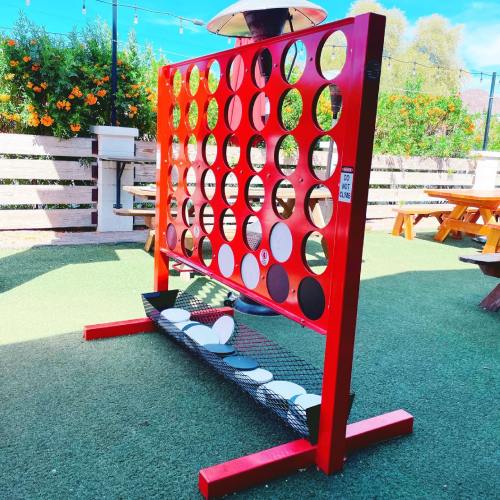 A large red Connect Four game set outdoors, with a grassy area and picnic tables in the background.