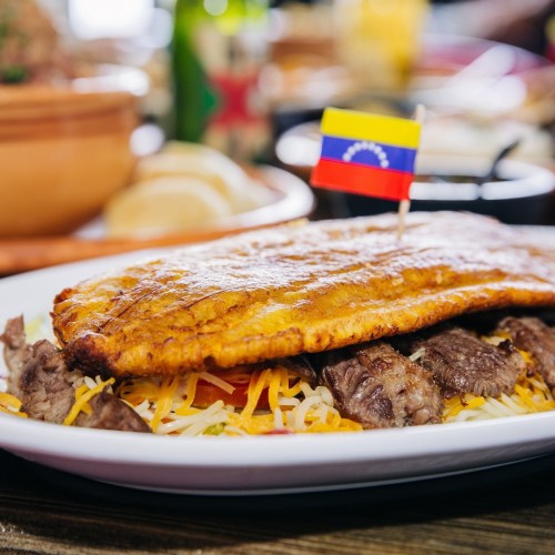 A plate of Venezuelan food featuring a large fried fish, beef, cheese, and a small flag of Venezuela on top.
