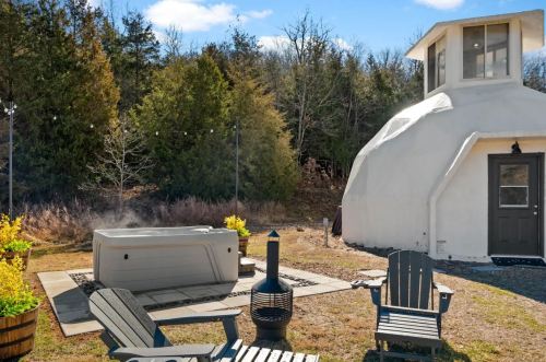 A cozy outdoor space featuring a hot tub, chairs, and a unique dome-shaped structure surrounded by trees.