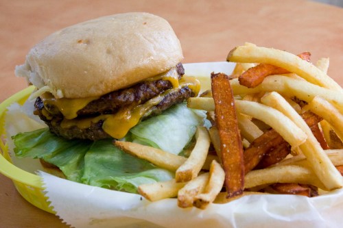 A cheeseburger with two patties and lettuce, served with a side of golden fries on a yellow plate.