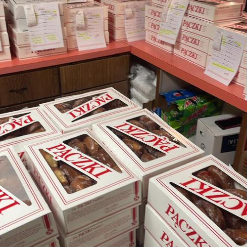 Boxes of paczki stacked on a counter, with some labeled and a colorful assortment of items in the background.