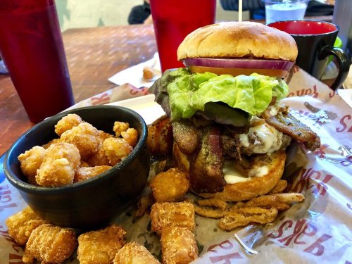 A hearty burger with lettuce, bacon, and mayo, served with a side of tater tots and crispy onion rings.