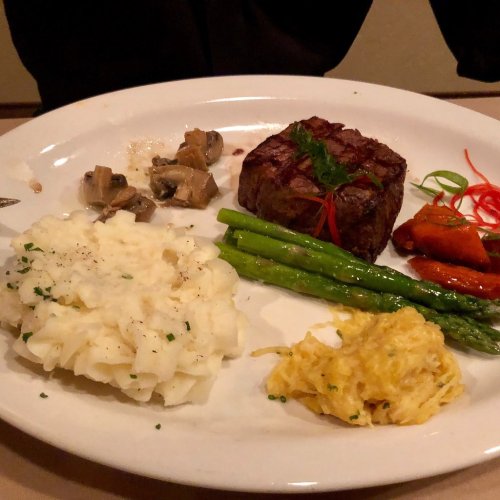 A plate featuring a steak, mashed potatoes, asparagus, sautéed mushrooms, and a side of squash.
