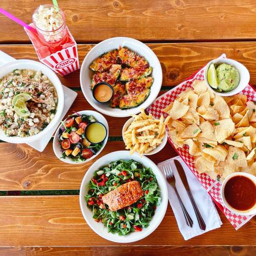 A vibrant spread of food including salads, nachos, fries, and a drink on a wooden table.