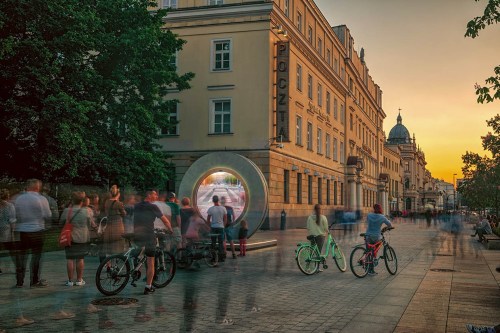 A bustling street scene at sunset, with people and bicycles near a circular sculpture.