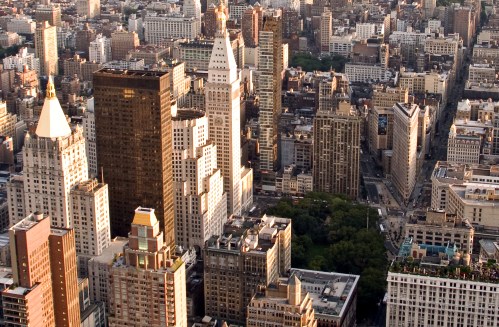 Aerial view of a bustling city skyline with diverse architectural styles and green spaces among tall buildings.