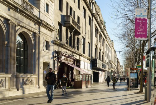 A bustling city street with pedestrians, historic buildings, and banners on a clear day.