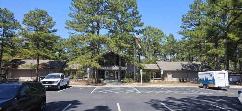 A parking lot in front of a building surrounded by trees, with a clear blue sky above.