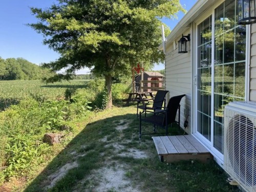 A sunny outdoor area with chairs beside a house, overlooking a green field and trees.