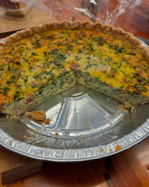 A sliced quiche with a golden crust, filled with spinach and other ingredients, in a silver pie dish.