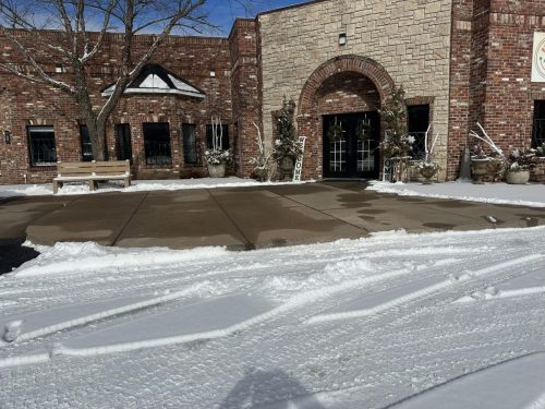 A snowy scene outside a brick building with a clear entrance and tire tracks on the ground.