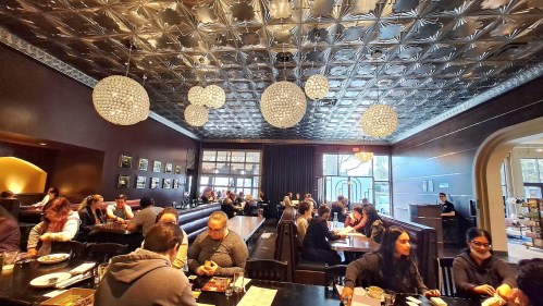 A bustling restaurant interior with a decorative ceiling, stylish lighting, and patrons enjoying meals at tables.