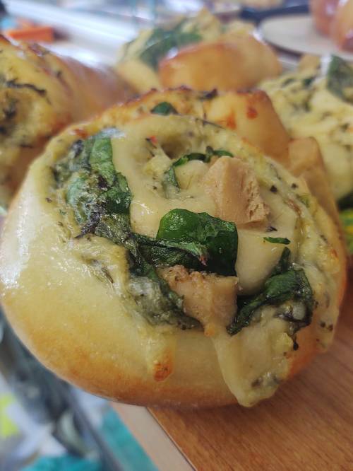 A close-up of a savory roll filled with spinach, chicken, and herbs, showcasing a golden-brown crust.
