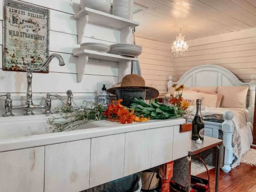 A cozy room featuring a vintage sink, flowers, a hat, and a bed with soft linens under a chandelier.