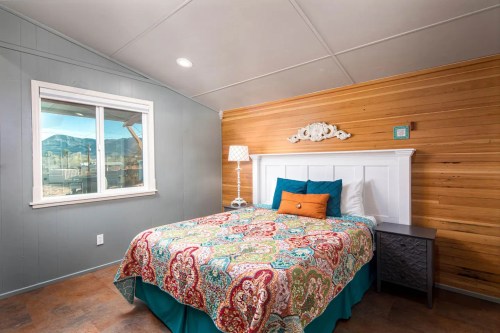 Cozy bedroom with a colorful patterned bedspread, wooden accent wall, and a window showcasing mountain views.