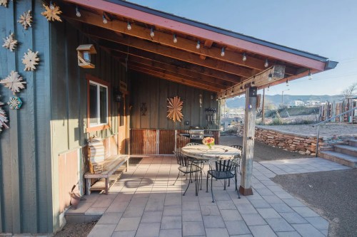 A cozy outdoor patio with a table and chairs, surrounded by rustic decor and a scenic view.
