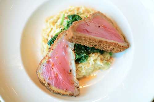 A plate featuring two slices of seared tuna on a bed of creamy risotto and sautéed greens.