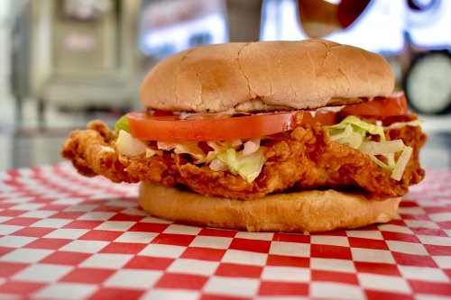 A close-up of a crispy fried chicken sandwich with lettuce, tomato, and mayonnaise on a red and white checkered paper.