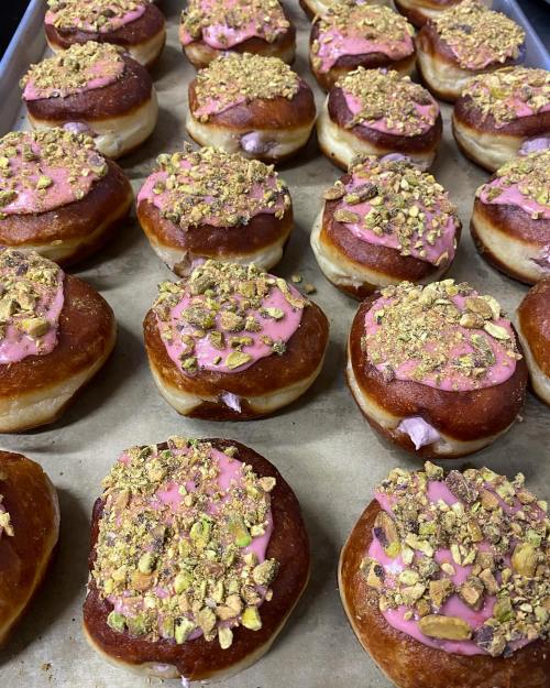 A tray of freshly baked donuts topped with pink icing and crushed pistachios.