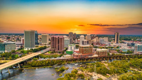 Aerial drone view of downtown Richmond, Virginia, showing the city skyline with high-rise buildings, streets, and the surrounding urban landscape under a clear sky.