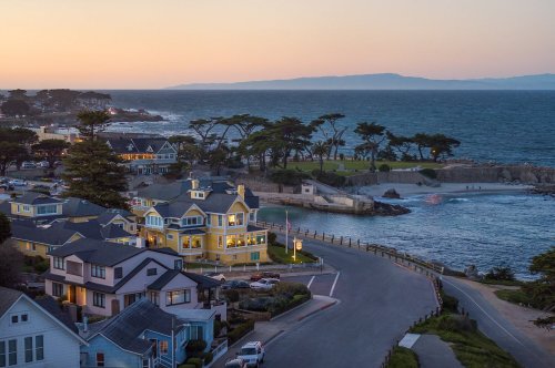 Coastal view at sunset featuring colorful houses, a winding road, and a serene ocean landscape.