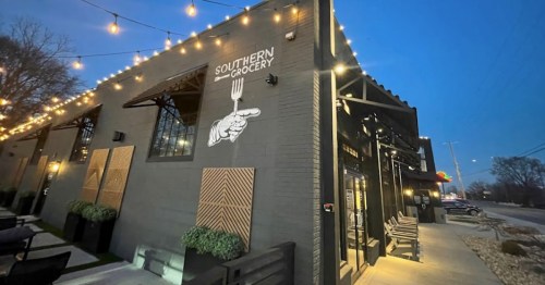 Exterior of Southern Grocery at dusk, featuring string lights and a hand pointing to a fork on the wall.