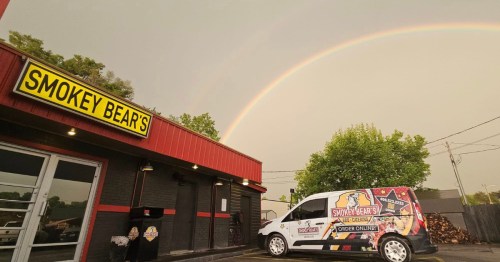 Exterior of Smokey Bear's BBQ, a red building with a rainbow overhead and a catering truck nearby