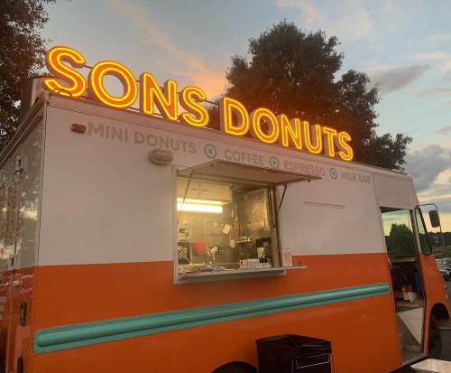 A colorful food truck named "Sons Donuts" with a glowing sign, offering mini donuts, coffee, and espresso.