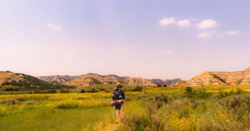 Hiker making their way towards the dry foothills in South Dakota under a light purple sky.