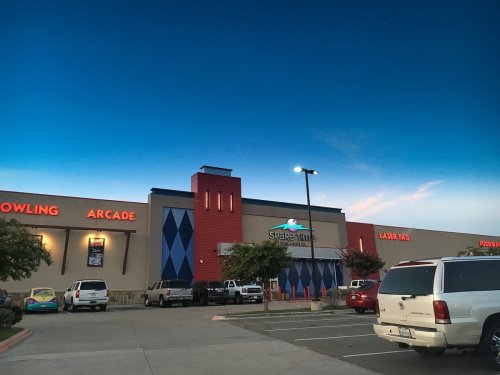 Exterior of a family entertainment center featuring bowling, arcade games, and laser tag, under a twilight sky.