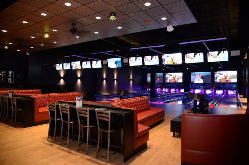 A modern bowling alley interior with seating, multiple screens, and vibrant lighting.