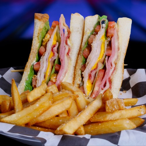 A stacked sandwich with layers of meat, cheese, lettuce, and tomato, served with a side of golden French fries.