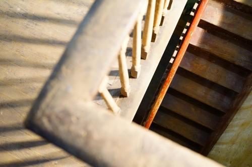 A wooden staircase viewed from above, featuring a railing and a mix of light and shadow on the steps.