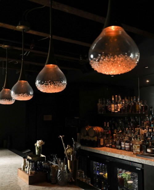 A dimly lit bar featuring elegant pendant lights and a well-stocked shelf of various spirits.
