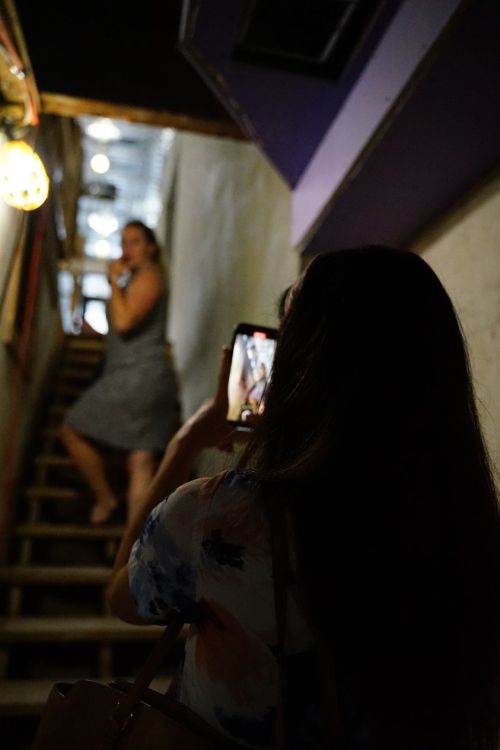 A person takes a photo of another person on a staircase, with warm lighting and a cozy atmosphere.