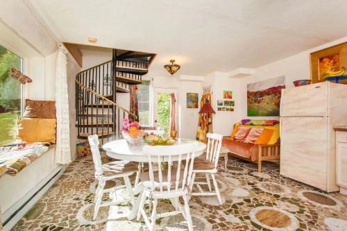 Cozy kitchen area with a round table, spiral staircase, and colorful decor in a bright, inviting space.