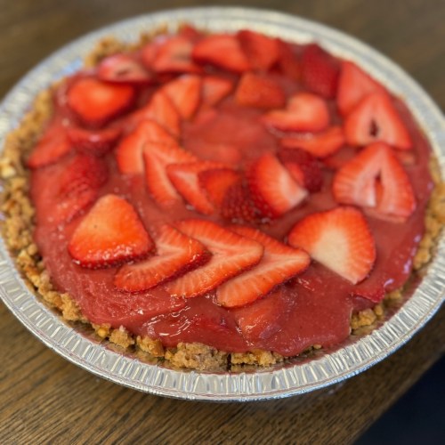 A strawberry pie with a glossy red filling and fresh strawberry slices on top, in a silver pie dish.