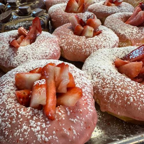 A tray of pink frosted donuts topped with fresh strawberries and dusted with powdered sugar.