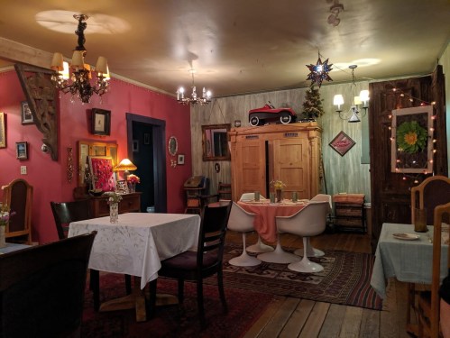 Cozy restaurant interior with colorful walls, vintage decor, tables, and a classic car display. Warm lighting creates a welcoming atmosphere.