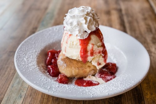 A dessert featuring a scoop of ice cream topped with whipped cream and strawberry sauce, served on a plate with strawberries.
