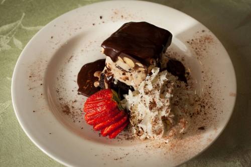 A dessert plate featuring a chocolate-covered ice cream square, topped with whipped cream and a fresh strawberry.