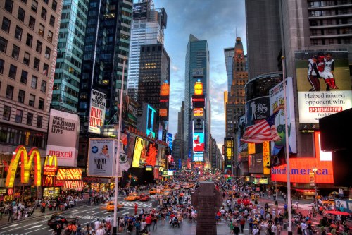 A bustling Times Square filled with people, bright billboards, and iconic landmarks under a dramatic sky.