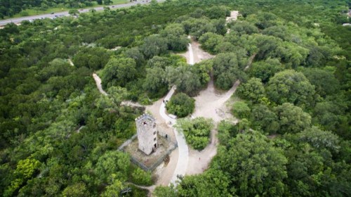 Aerial view of a stone tower surrounded by lush greenery and winding paths in a park setting.