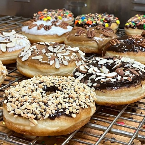 A variety of decorated donuts on a cooling rack, topped with nuts, chocolate, and colorful sprinkles.