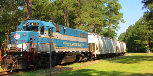 A blue and yellow vintage train engine parked beside a white freight car in a wooded area.