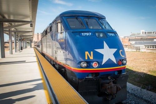 A blue and yellow train with a star logo is parked at a modern train station platform under a clear sky.