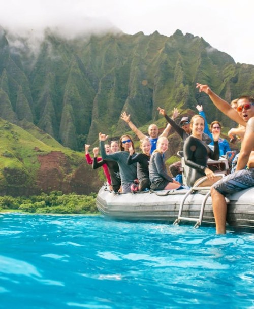 A group of people on a boat, smiling and enjoying a scenic view of lush green mountains and blue water.